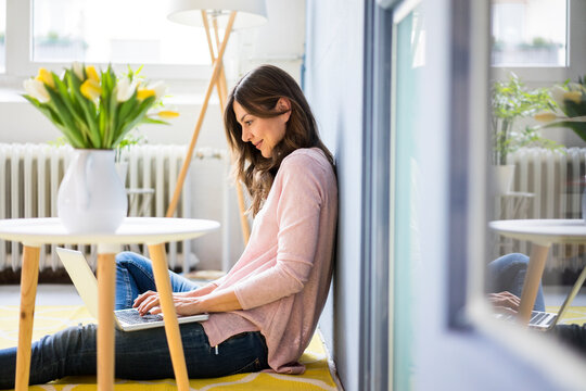 Smiling woman sitting on floor next to table with tulips using laptop