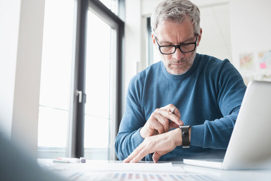 Mature man sitting in office working with laptop and smart watch