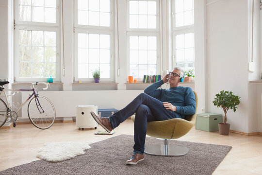 Relaxed mature man at home sitting in chair listening to music