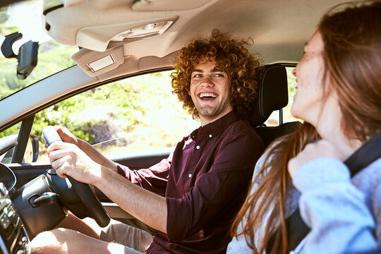 Laughing young man driving car looking at his girlfriend