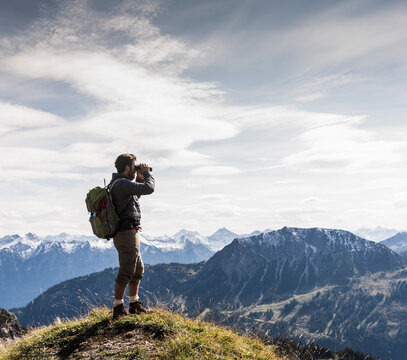 Austria, Tyrol, young man standing in mountainscape looking at view with binoculars