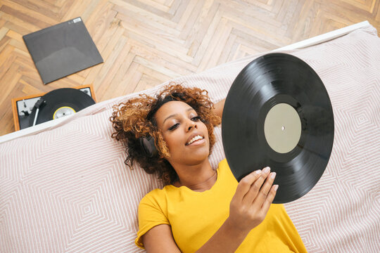 Young woman lying on bed listening to music with headphones and record player