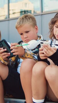 Tenager schoolchildren of two Caucasian girls and boys holding mobile phone and browsing while sitting on stair during school break, oudoors . Slow motion