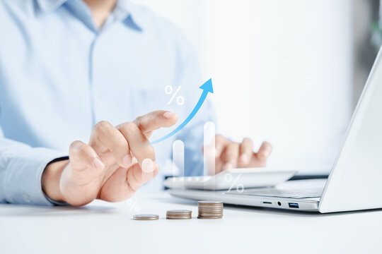 Business professional using laptop and calculator with financial growth chart overlay and stacked coins on desk, fintech investment analytics concept, soft blue corporate tone, modern digital banking
