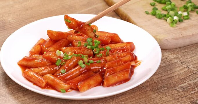 Korean dish tteokbokki in red sauce on a plate, tteokbokki is being taken with chopsticks.
