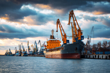 Obraz premium Containers are loaded and unloaded at the cargo sea port. Cranes move goods while large ships dock along the waterfront. Workers manage operations on the ships and wharf