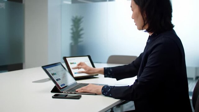 A gender-neutral professional in business-casual attire, focused at a minimalist desk with laptop, tablet, and smartphone in a contemporary office. Dolly video to close-ups, shallow DOF. Concept of