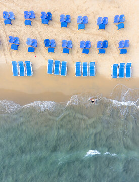 Aerial view of Bat Yam beach with blue sunbeds and chairs on the golden sand near turquoise water with a person swimming in the waves Bat Yam, Center District, Israel.