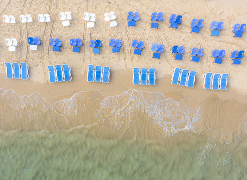 Aerial view of rows of blue and white sunbeds on the sand near the gentle waves of the Mediterranean Sea at Bat Yam beach in Bat Yam, Center District, Israel.