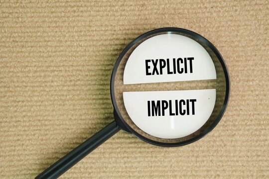 Magnifying glass with explicit and implicit words. explicit and implicit are opposites. Explicit describes something as being expressed directly without anything being implied