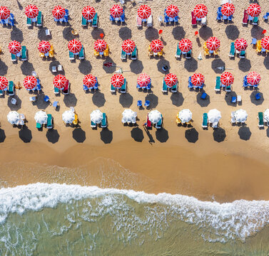 Aerial view of Bat Yam beach with rows of red and white umbrellas on the sand and waves crashing on the shore in Bat Yam, Center District, Israel.