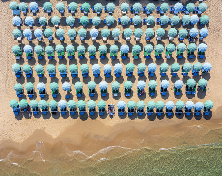 Aerial view of Bat Yam beach with rows of turquoise and light blue umbrellas on the sand by the sea with people relaxing under the sunshades Bat Yam, Center District, Israel.