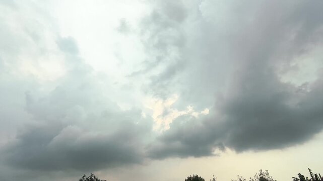A dramatic overcast sky filled with heavy dark gray and white storm clouds above a faint tree line. Handheld shot footage
