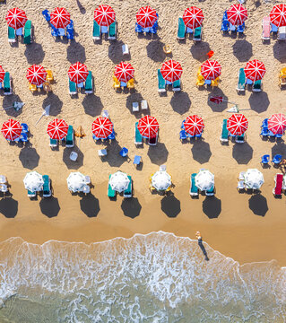 Aerial view of Bat Yam beach featuring rows of red and white umbrellas and sunbeds on golden sand with waves washing onto the shore Bat Yam, Center District, Israel.