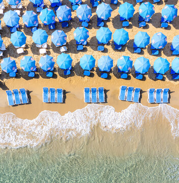 Aerial view of Bat Yam beach featuring rows of blue umbrellas and sun loungers on golden sand by the turquoise sea Bat Yam, Center District, Israel.