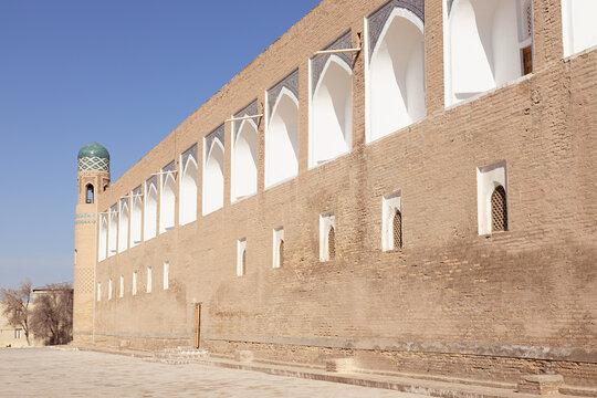 Madrasa of Muhammad Amin Khan in Khiva with its massive brick wall and minaret with turquoise dome. Ideal for travel guides, heritage publications, and Central Asian tourism content.