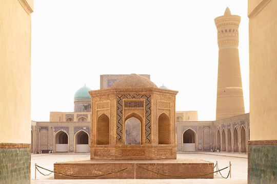 Kalyan Mosque courtyard with ornate pavilion and Kalyan Minaret in Bukhara, Uzbekistan. Historic Islamic architecture framed by arched galleries and turquoise domes, ideal for travel and heritage.