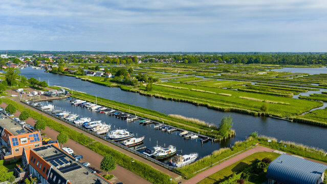 Aerial view of the Oosterdel nature reserve with lush green fields and a marina filled with boats in Broek op Langedijk, Noord-Holland, Netherlands.
