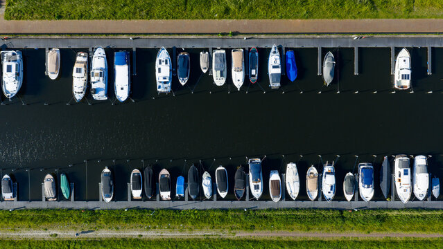 Aerial view of boats moored at the Oosterdel marina with parallel docks and green banks in Broek op Langedijk, Noord-Holland, Netherlands.