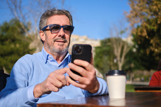 close up shot of Senior man using smartphone enjoying coffee outdoors in barcelona park