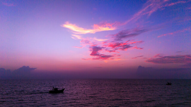 Aerial view of a fishing boat on the calm sea under a vibrant purple and pink sunset sky at Varca Beach, SOUTH GOA, Goa, India.