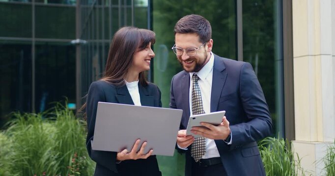 Happy laughing business coworkers having a friendly conversation in a modern office, holding laptop and tablet