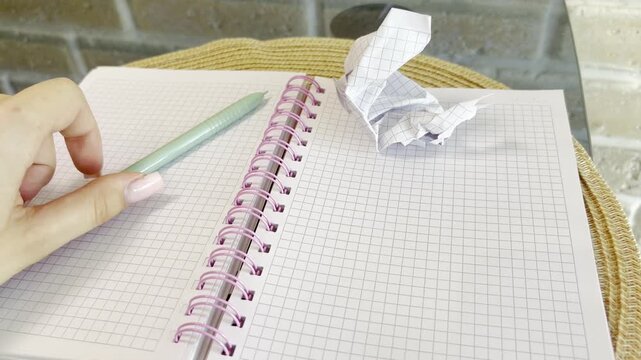 Frustrated woman experiencing writer's block crumbling paper and throwing a pen on an empty spiral notebook, feeling stressed, anxious and without creative ideas