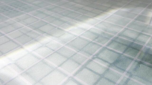 Abstract sunbeam moving across a textured glass surface creating a play of light and shadow, highlighting the geometric grid pattern of the windowpane in a serene mood