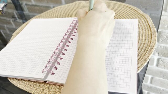 Woman's hand writing a note on a grid paper notebook, getting frustrated, and then ripping out the page to start over on a fresh blank sheet
