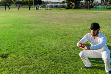 Naklejka premium Man squatting low on wide mown grass field, wearing black cap and athletic shoes, copy space