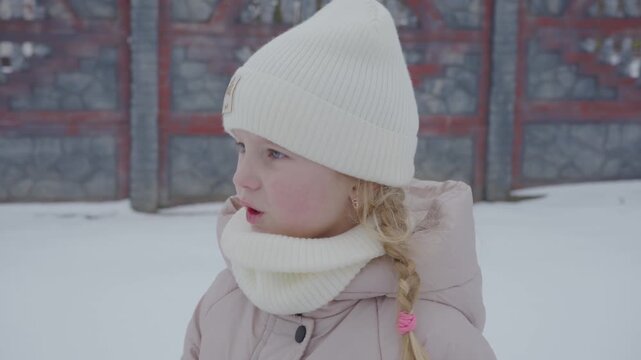 Little girl with a braid wearing winter clothes outside, Portrait of a little girl in a white knitted hat and scarf standing outdoors in winter.