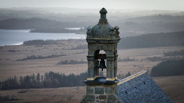 Aerial view of the stone bell tower of Mont Saint-Michel de Brasparts overlooking misty hills and valleys of the Armorique Regional Natural Park in Saint-Rivoal, Bretagne, France.