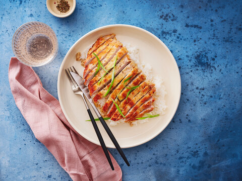 This dish features a seared chicken breast served over a bed of rice, garnished with green onions. Ideal for menu designs, meal prep planning, and healthy eating campaigns