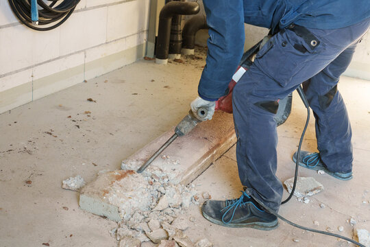 Worker using jackhammer to break concrete floor during renovation