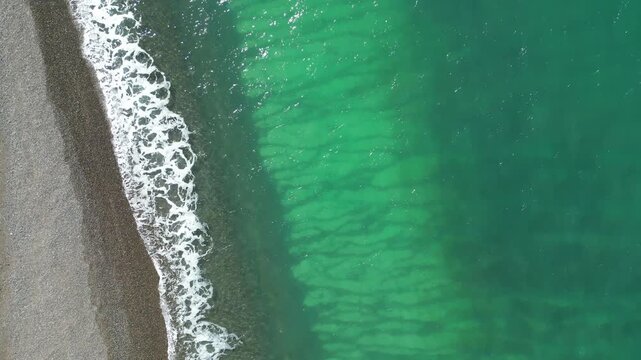 Aerial top down view of turquoise ocean waves meeting pebble beach on Peninsula Valdes coast in Patagonia Argentina