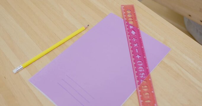 Slow motion classroom desk shot moves across purple notebook, pink ruler, yellow pencil, wooden surface, back to school first day supply setup for primary learning routine and homework preparation