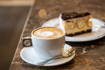 Obraz premium A warm cup of frothy cappuccino sits on a dark marble cafe table alongside a delicious slice of berry-topped cheesecake.