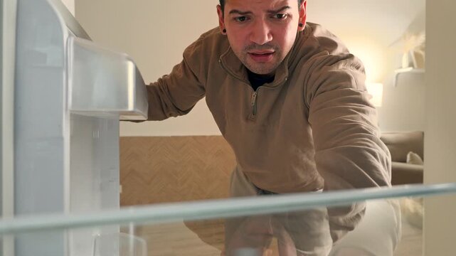 young man opening an empty refrigerator looking disappointed and finding only one single egg, inside pov shot of hungry person looking for food in kitchen