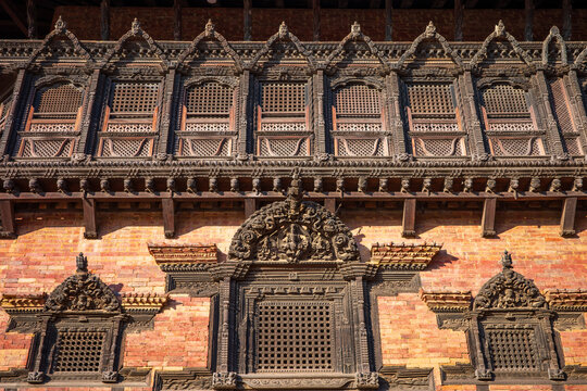 Detailed view of beautifully carved Newari wooden windows on a historic brick building in Bhaktapur, Nepal. This architectural facade showcases traditional craftsmanship, cultural heritage