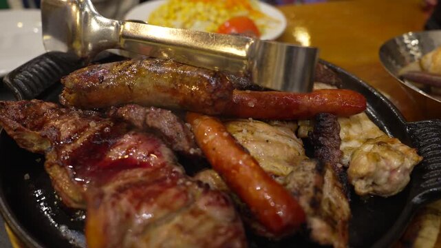 Mixed grilled meat platter with sausages, pork, and beef served on hot iron plate in Madrid, Spain, close up food shot inside traditional Spanish restaurant.