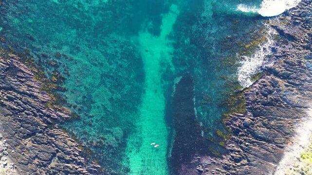 Drone aerial landscape of ocean waves crashing along rocky reef coastline with people waiting on watercraft in a sandy cove at Malua Bay South Coast Eurobodalla NSW Australia nature and outdoors