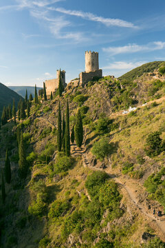 Tourists hiking along a mountain trail toward medieval stone castle ruins, representing travel and exploration in nature at Four Lastours castle, Languedoc-Roussillon, France.