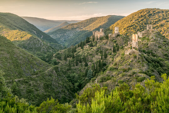 Medieval castle ruins stand on rocky hillsides surrounded by lush valleys and greenery, representing a historic travel destination in the Languedoc-Roussillon region, Four Lastours, France.