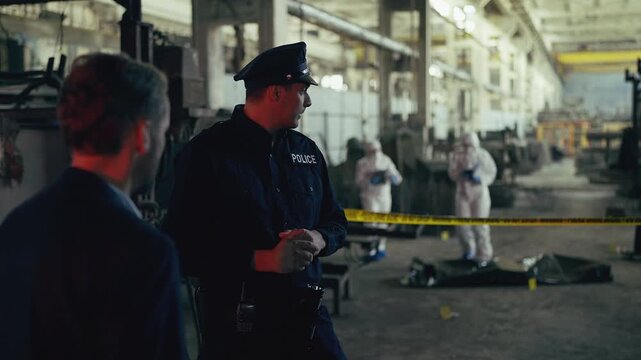 Police officer and male detective discussing crime scene at industrial plant