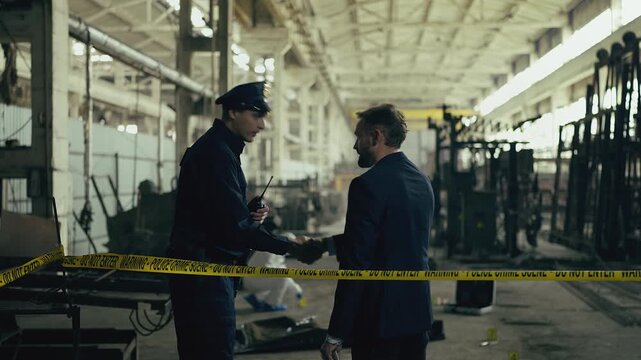 Police officer allowing detective through police barrier tape at industrial site