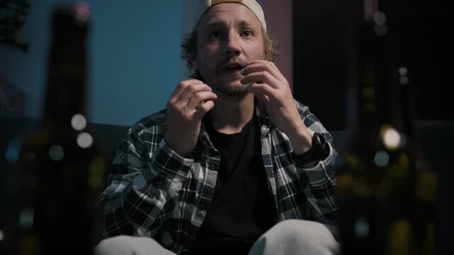 Close up emotional reaction of disappointed sports fan after losing game while watching television at home. Frustrated man sits on couch before drinking beer during late evening.