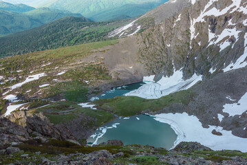 Awesome top view from rock precipice edge to two turquoise alpine lakes with ice floes in stone mountain cirque. Harsh landscape with small creek between two green icy lakes in rocky stony terrain. © Daniil