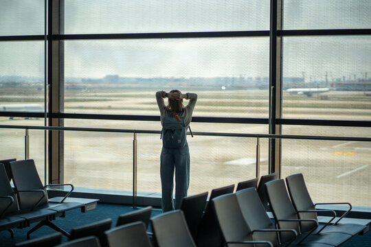 Upset woman traveler standing in airport terminal holding head after missing boarding time. Stressed, overwhelmed due to delayed, canceled, or rescheduled flight. Emotional pressure in air travel.