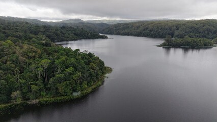 Fototapeta premium Aerial view of Rocky Creek Dam reservoir surrounded by lush rainforest and misty hills in New South Wales, Australia