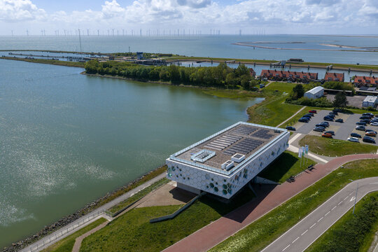 Kornwerderzand, Netherlands - 14 May 2026: Aerial view of the Afsluitdijk Wadden Center building with its hexagonal facade overlooking the water and a distant offshore wind farm.